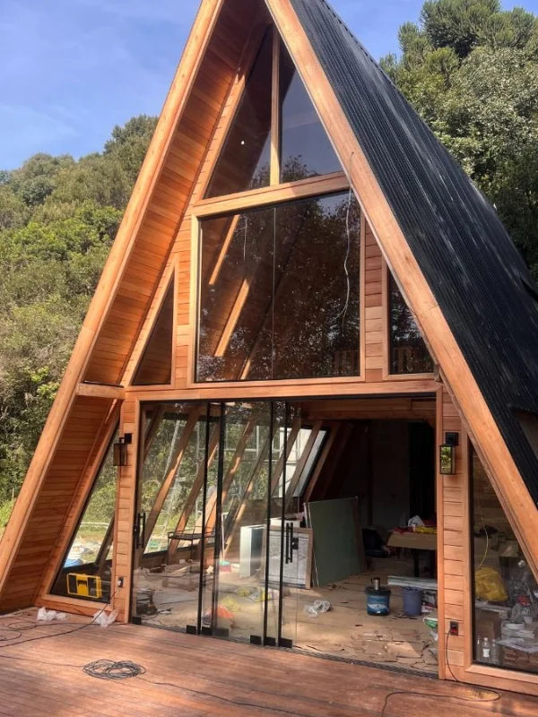 Chalé A-frame em construção com grandes portas de vidro sendo instaladas