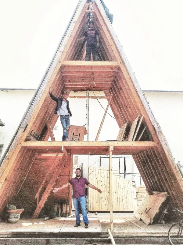 Estrutura A-frame em construção com trabalhadores instalando painéis vermelhos